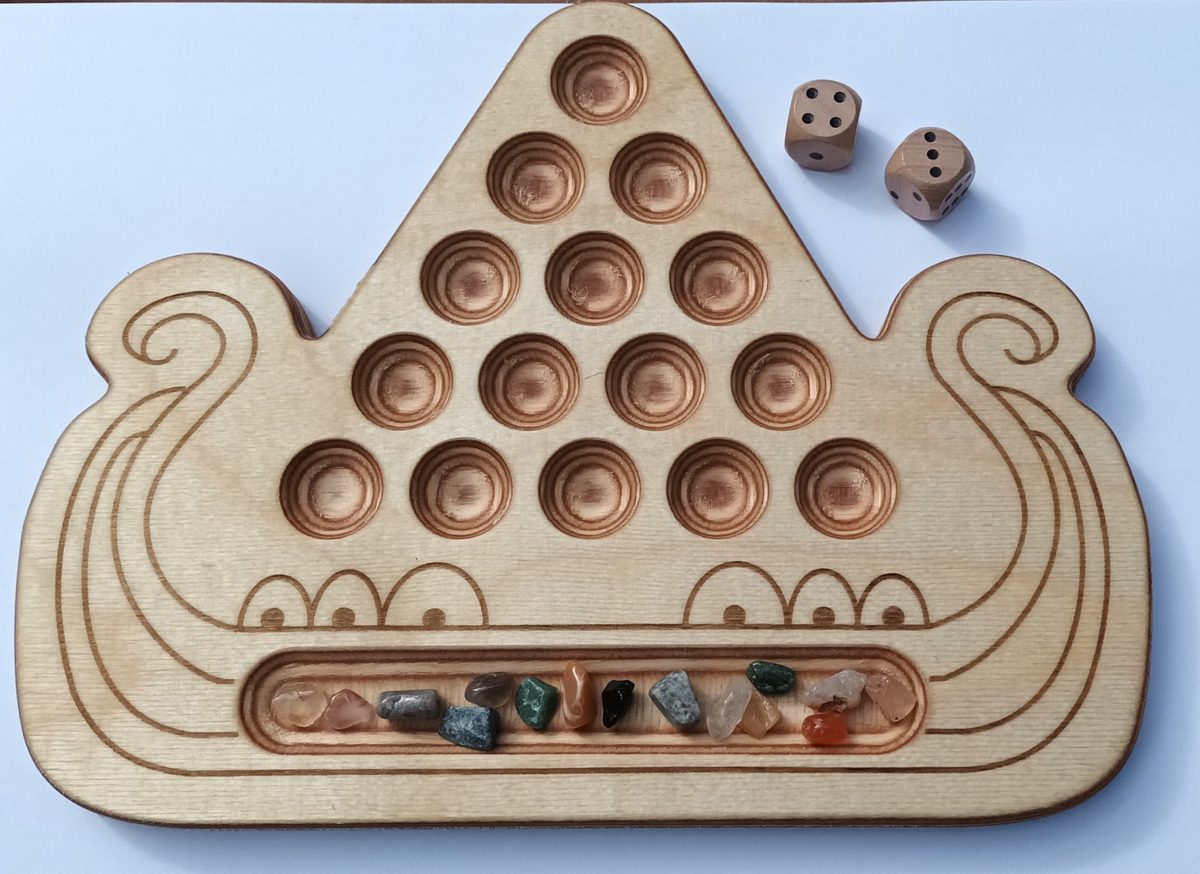 Spielbrett von Kaperfahrt in Form eines Wikinger-Langschiffs aus hellem Holz: ein Dreieck aus 15 runden Mulden, darunter im Schiffsbauch das längliche Vorratsfeld mit bunten Glassteinen, daneben zwei Holzwürfel.